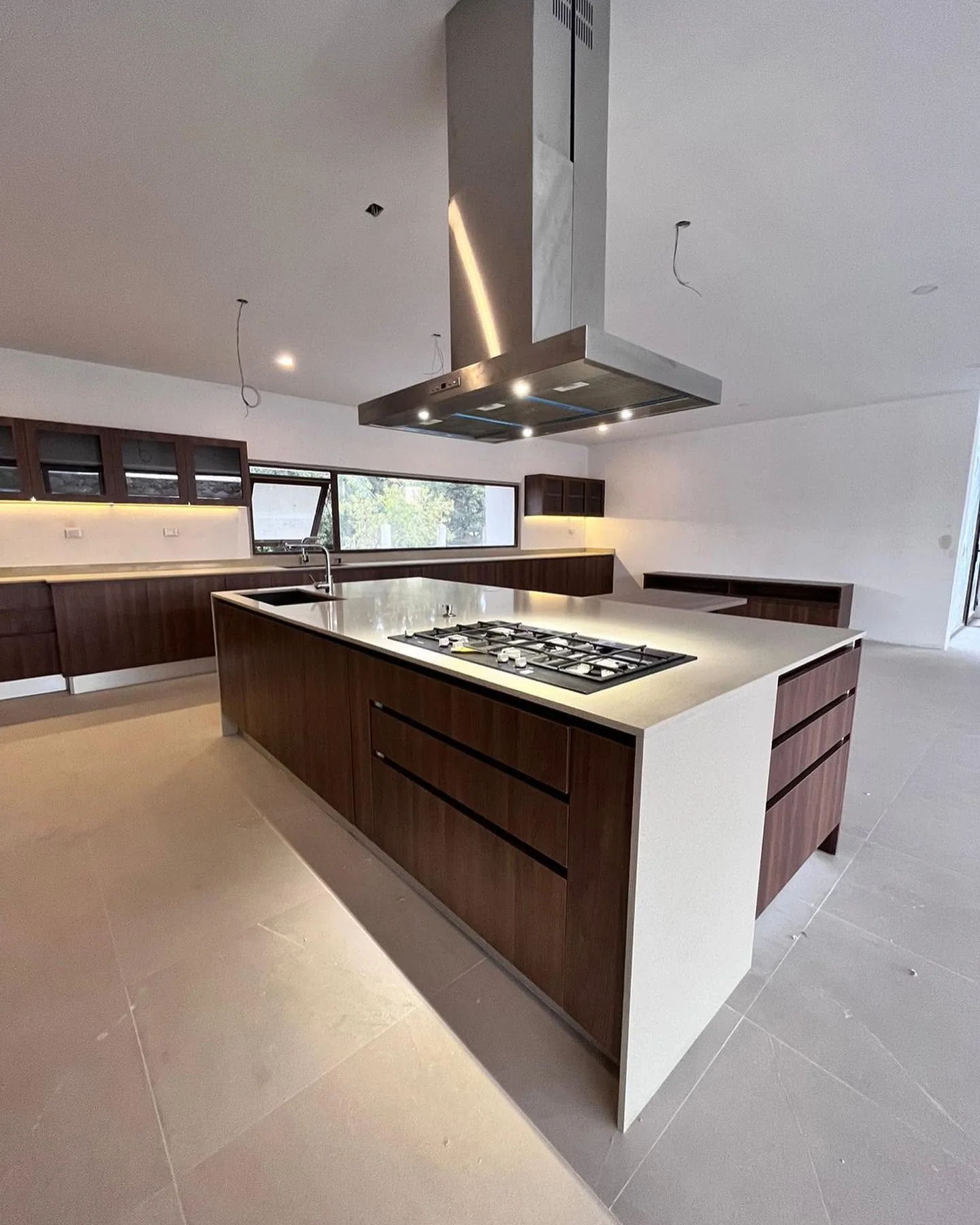 Isla de cocina con mobiliario de madera, cubierta clara y campana de acero inoxidable