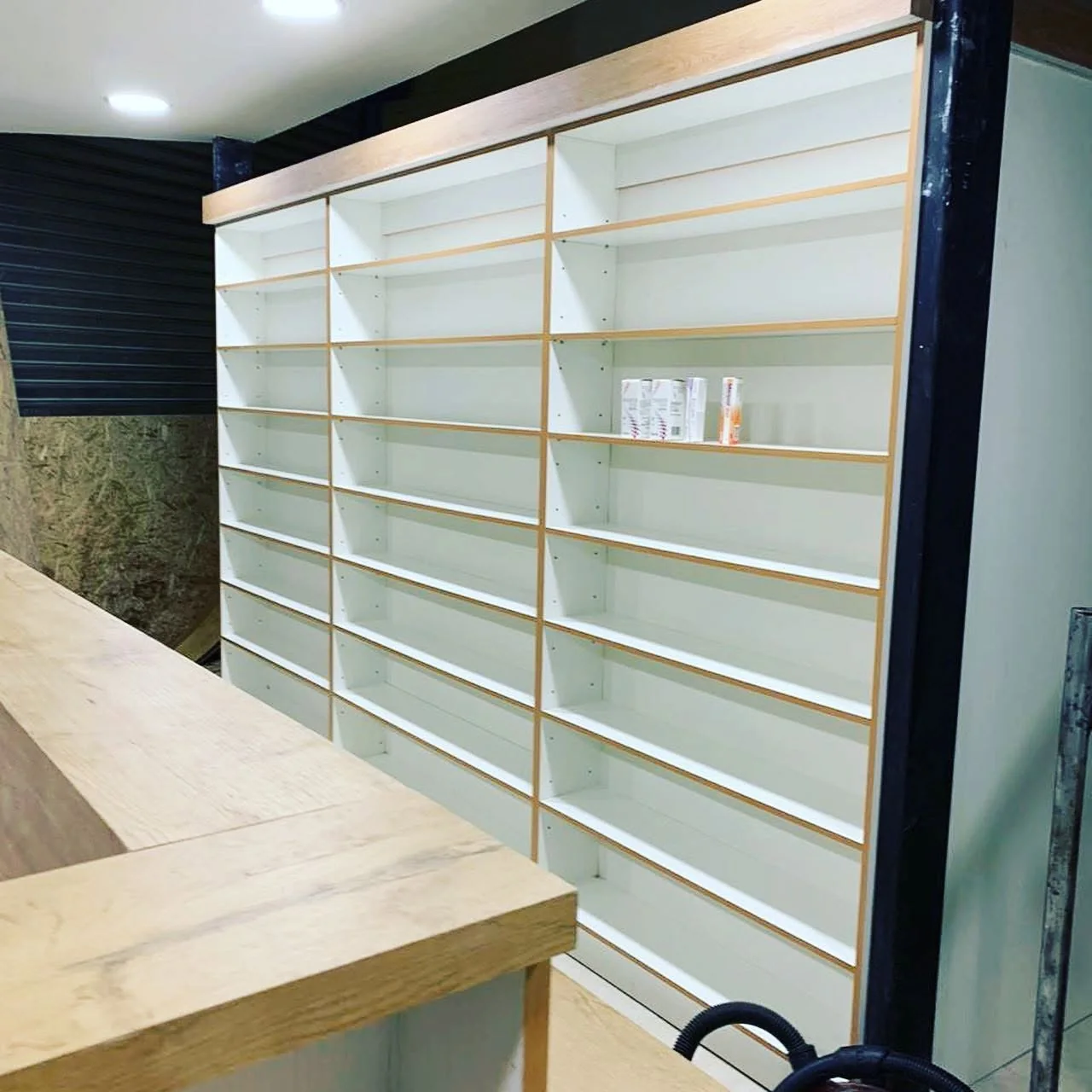 Mobiliario farmacéutico perimetral con repisas blancas y terminaciones en madera
