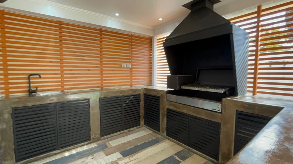 Quincho exterior con parrilla integrada, mobiliario metálico y revestimiento de madera