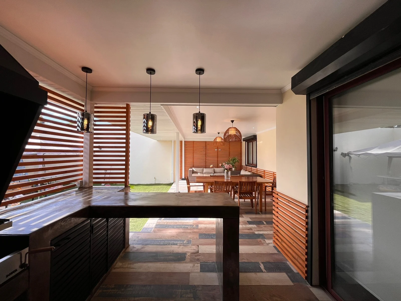 Vista general del quincho exterior con barra, comedor, iluminación colgante y revestimientos de madera